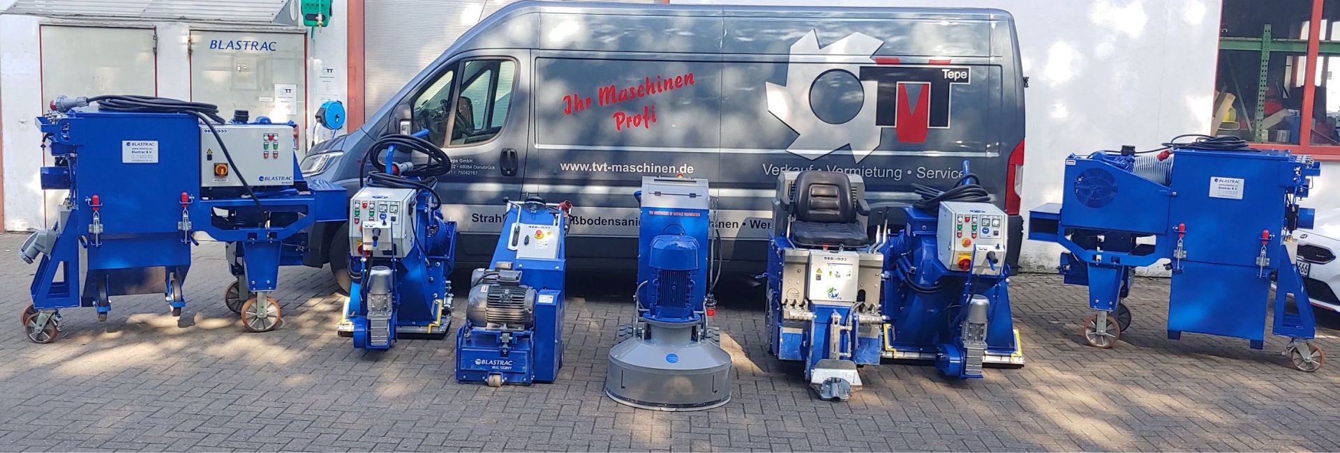 Eine Reihe blauer Blastrac-Maschinen, die vor einem Servicewagen ausgestellt sind und für die Bodenvorbereitung und Oberflächenbehandlung verwendet werden.